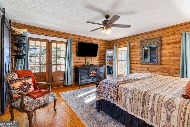 bedroom with ceiling fan, wood-type flooring, a textured ceiling, and log walls