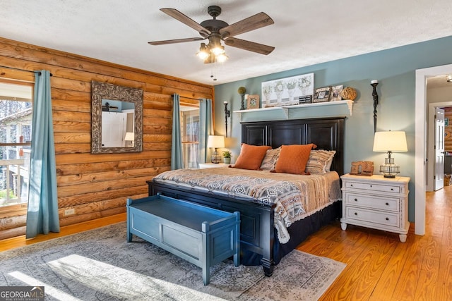 bedroom with ceiling fan, a textured ceiling, log walls, and light hardwood / wood-style flooring