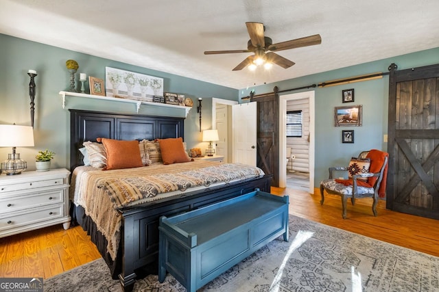 bedroom with a barn door, light hardwood / wood-style floors, ceiling fan, and connected bathroom