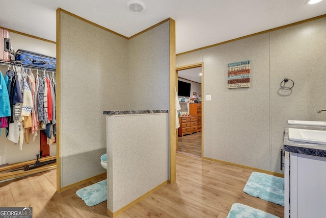 bathroom featuring toilet, vanity, wood-type flooring, and ornamental molding