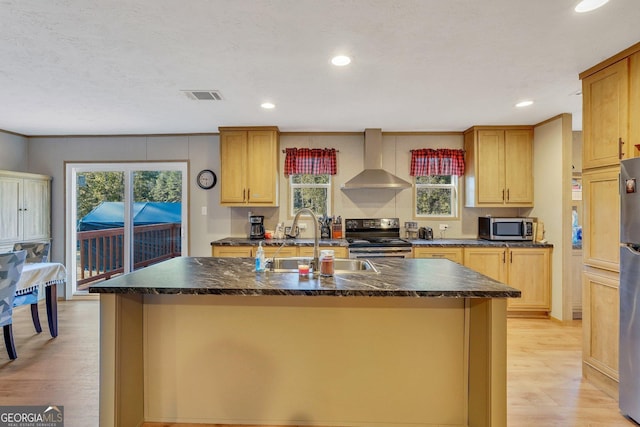 kitchen featuring wall chimney exhaust hood, sink, appliances with stainless steel finishes, and an island with sink