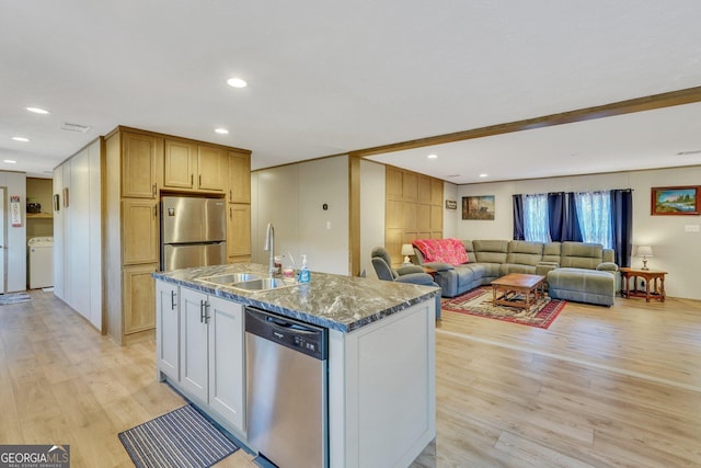 kitchen featuring white cabinets, sink, an island with sink, appliances with stainless steel finishes, and washer / dryer