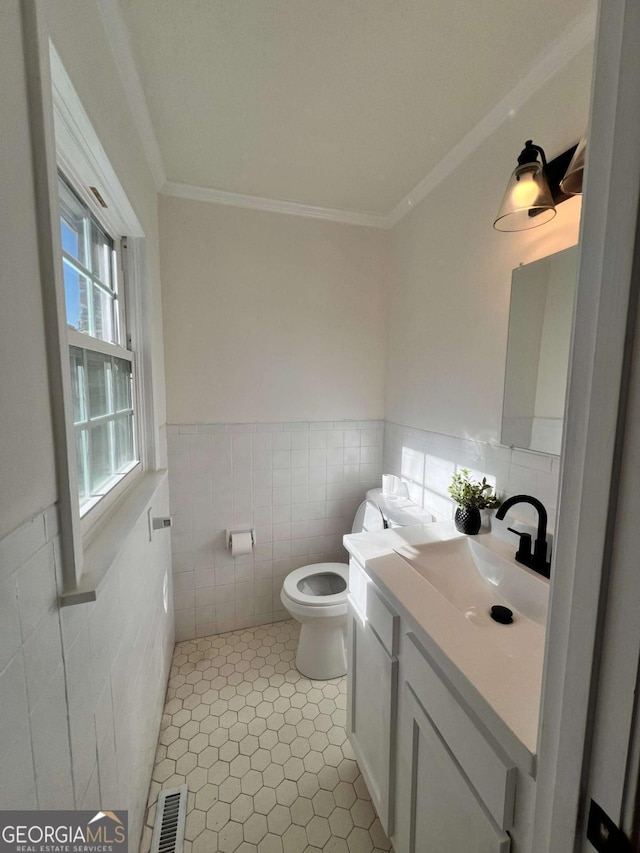 bathroom with tile patterned floors, crown molding, toilet, vanity, and tile walls