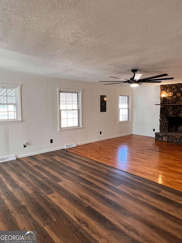 unfurnished living room with a textured ceiling, electric panel, dark hardwood / wood-style flooring, and a stone fireplace