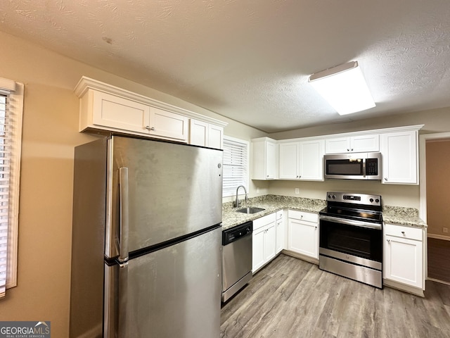 kitchen featuring white cabinets, sink, light wood-type flooring, light stone countertops, and appliances with stainless steel finishes