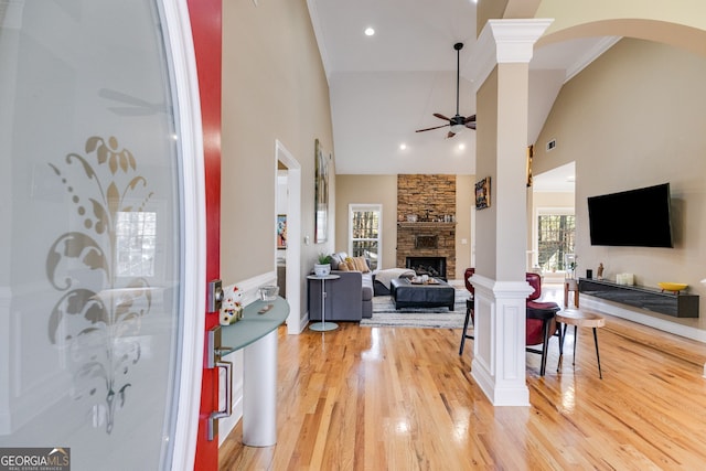 living room with a towering ceiling, hardwood / wood-style flooring, ornate columns, and a stone fireplace