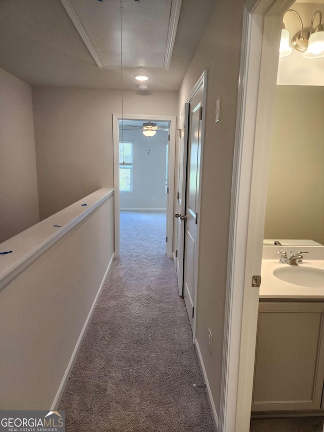 hall with light carpet, a raised ceiling, ornamental molding, and sink