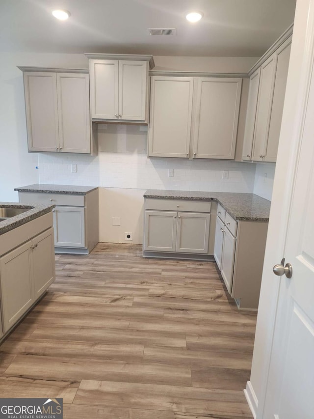 kitchen featuring tasteful backsplash, gray cabinetry, sink, light hardwood / wood-style flooring, and dark stone countertops