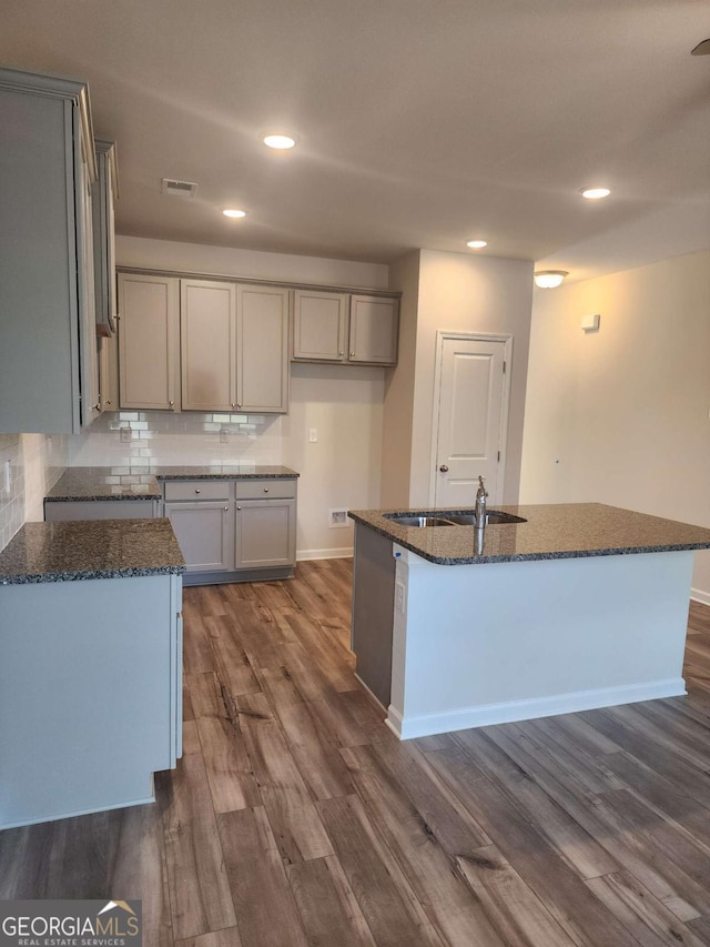 kitchen featuring sink, dark hardwood / wood-style floors, backsplash, gray cabinets, and a kitchen island with sink