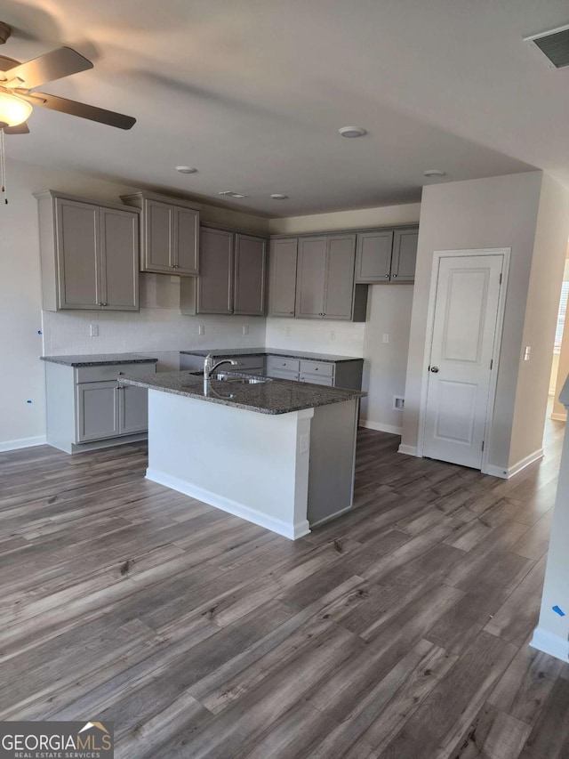 kitchen with gray cabinetry, ceiling fan, sink, dark hardwood / wood-style floors, and a center island with sink