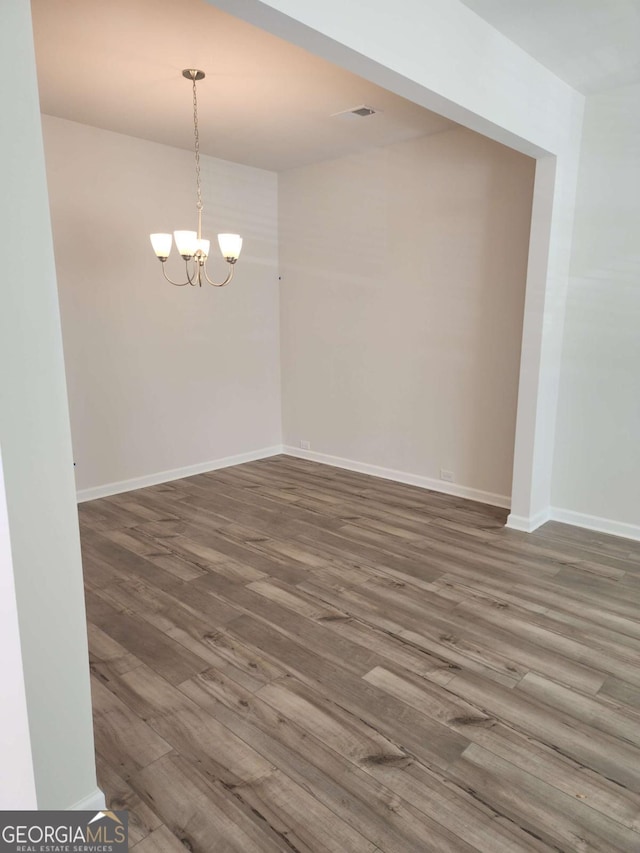 empty room with an inviting chandelier and dark wood-type flooring