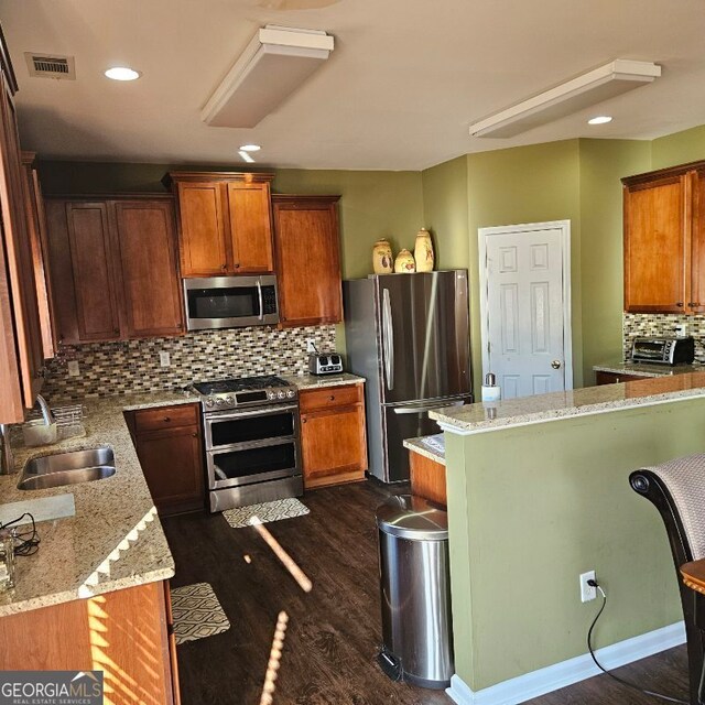 kitchen with light stone countertops, a breakfast bar, stainless steel appliances, and sink