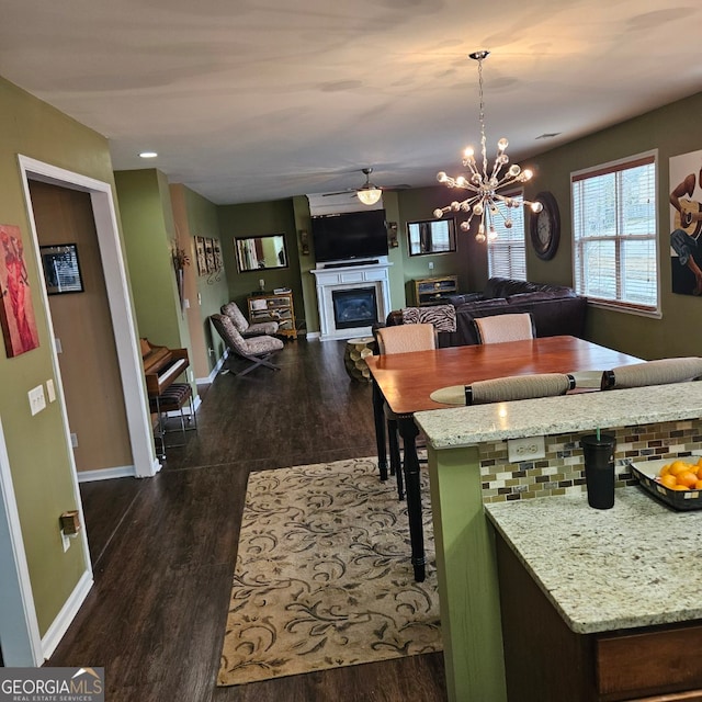 dining room with ceiling fan with notable chandelier and dark wood-type flooring