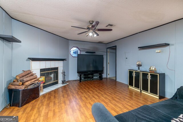 living room featuring ceiling fan, wood-type flooring, a textured ceiling, and a tile fireplace