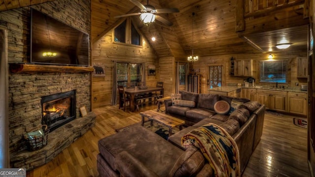 living room with high vaulted ceiling, ceiling fan with notable chandelier, wood-type flooring, a fireplace, and wood ceiling