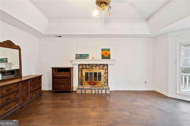 living room with dark hardwood / wood-style floors, a stone fireplace, a raised ceiling, and crown molding