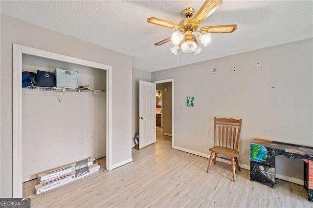 living area featuring ceiling fan, light hardwood / wood-style flooring, and a textured ceiling