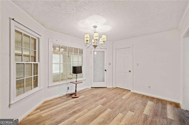 unfurnished dining area with light hardwood / wood-style flooring, a chandelier, a textured ceiling, and ornamental molding