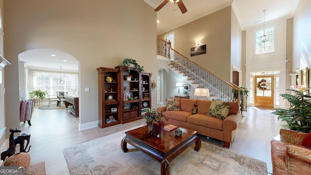 living room with ceiling fan, a towering ceiling, ornamental molding, and light hardwood / wood-style flooring