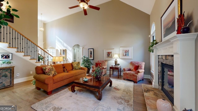 living room featuring ceiling fan, crown molding, high vaulted ceiling, light hardwood / wood-style flooring, and a fireplace