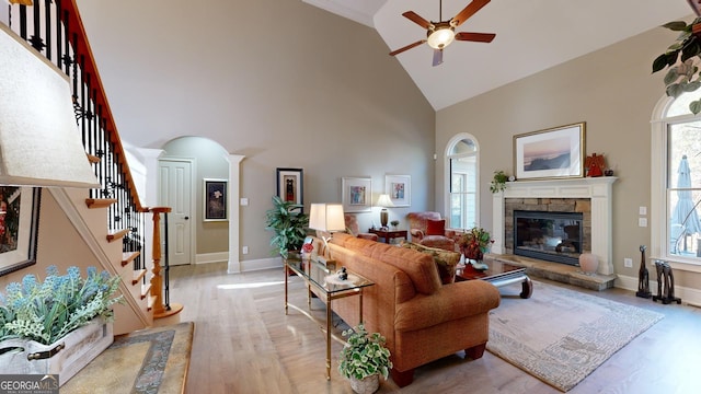 living room with light hardwood / wood-style flooring, high vaulted ceiling, ceiling fan, and a stone fireplace