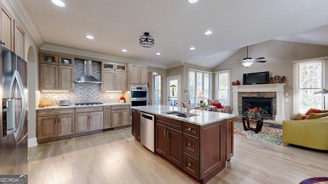 kitchen featuring appliances with stainless steel finishes, sink, wall chimney range hood, a fireplace, and an island with sink