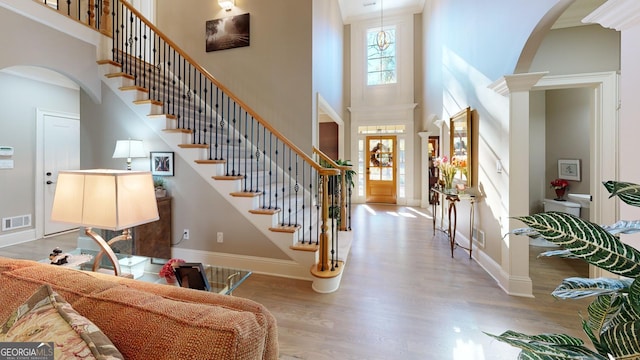 foyer entrance featuring a towering ceiling, decorative columns, and light hardwood / wood-style flooring