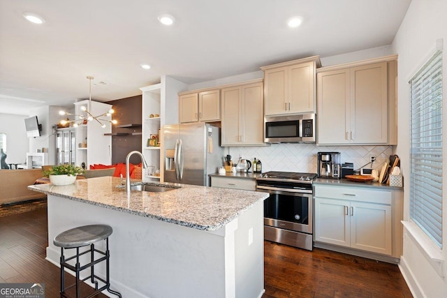 kitchen featuring appliances with stainless steel finishes, backsplash, sink, pendant lighting, and a center island with sink