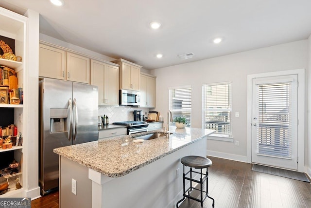 kitchen with cream cabinets, sink, stainless steel appliances, and a center island with sink