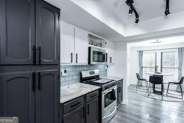 kitchen featuring light stone countertops, stainless steel appliances, light hardwood / wood-style floors, decorative backsplash, and white cabinets