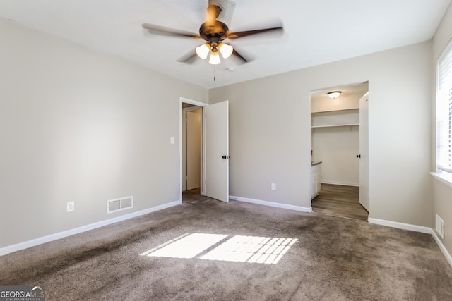 unfurnished bedroom with a walk in closet, ceiling fan, a closet, and carpet floors