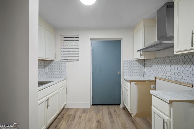 kitchen with sink, wall chimney exhaust hood, light wood-type flooring, tasteful backsplash, and white cabinetry