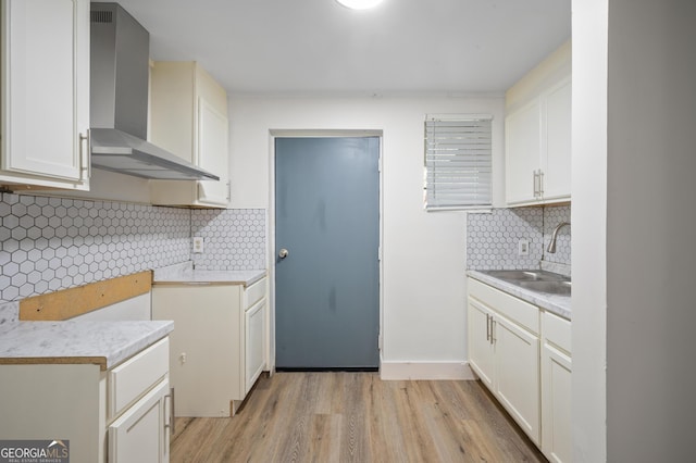 kitchen with wall chimney range hood, sink, light wood-type flooring, tasteful backsplash, and white cabinetry