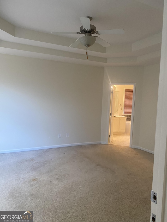 carpeted spare room featuring a tray ceiling and ceiling fan