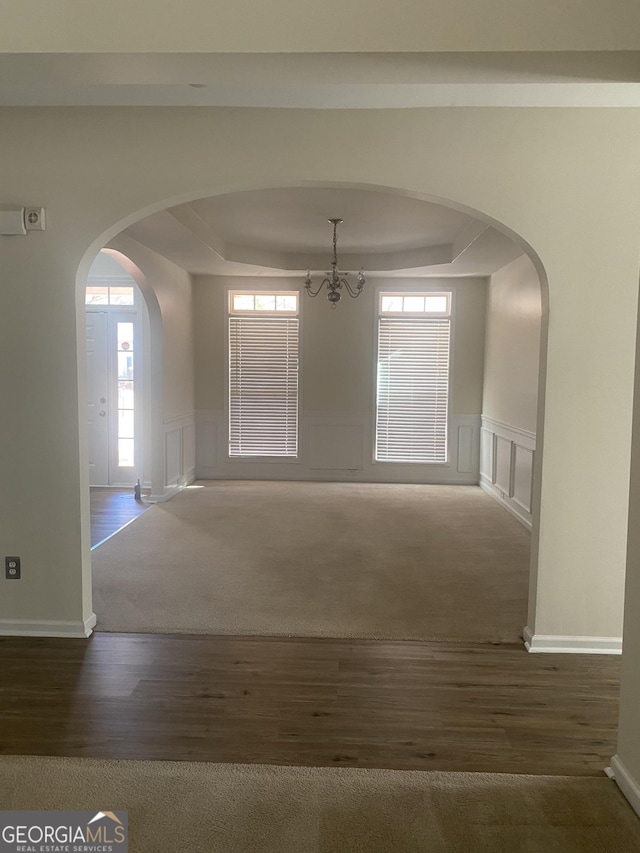 spare room featuring a chandelier, a tray ceiling, and dark carpet