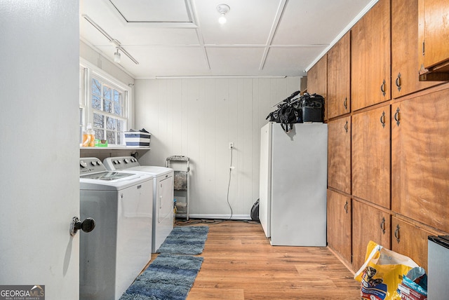 clothes washing area with cabinets, separate washer and dryer, light hardwood / wood-style flooring, and wooden walls