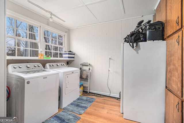 washroom with washer and clothes dryer, light hardwood / wood-style floors, cabinets, and wood walls