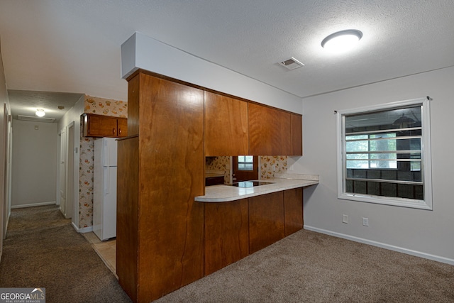 kitchen with kitchen peninsula, white fridge, light colored carpet, and a textured ceiling