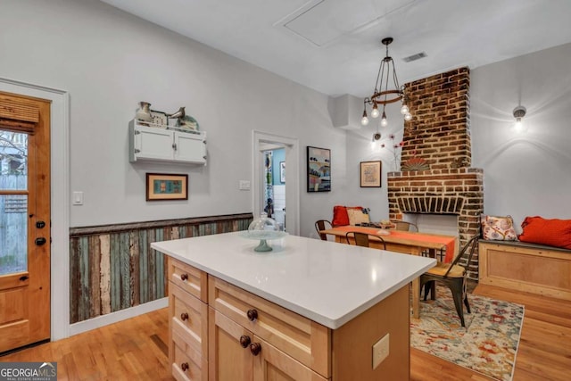 kitchen featuring light brown cabinetry, light wood-type flooring, a brick fireplace, a kitchen island, and hanging light fixtures