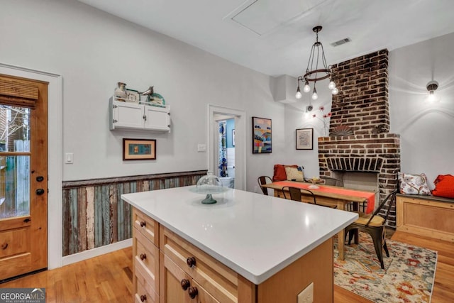 kitchen with a kitchen island, a brick fireplace, light hardwood / wood-style flooring, pendant lighting, and white cabinets