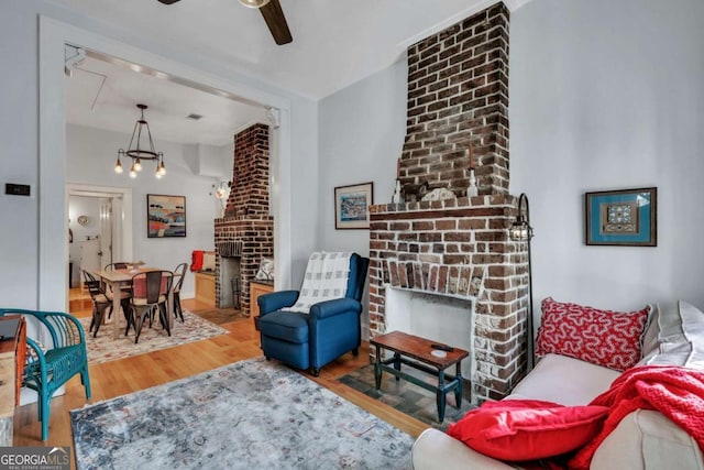 living room with hardwood / wood-style flooring, ceiling fan with notable chandelier, and a brick fireplace