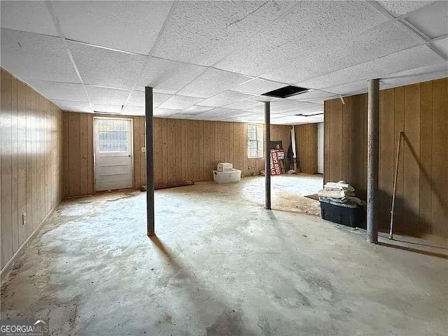 basement featuring a paneled ceiling and wood walls