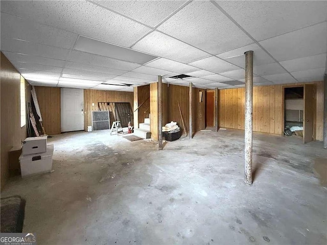 basement with a paneled ceiling and wood walls