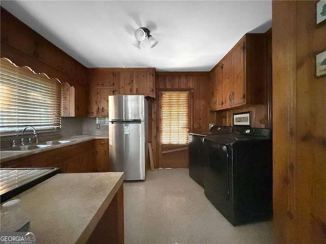 kitchen with wooden walls, washer / clothes dryer, sink, and stainless steel refrigerator