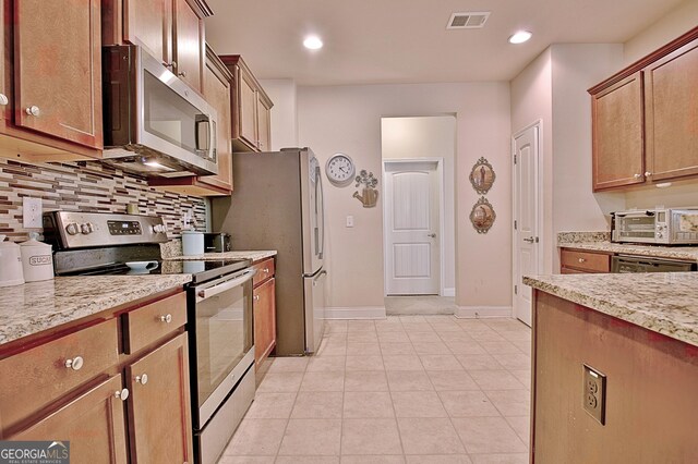 kitchen featuring tasteful backsplash, stainless steel appliances, light stone countertops, and light tile patterned floors