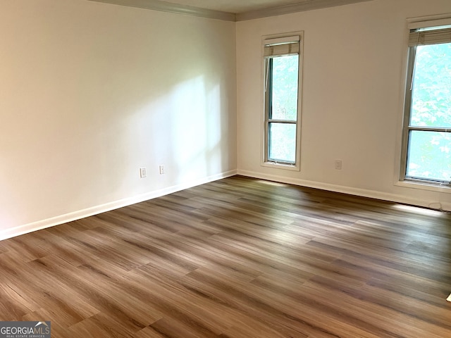 empty room featuring dark hardwood / wood-style flooring, a healthy amount of sunlight, and ornamental molding