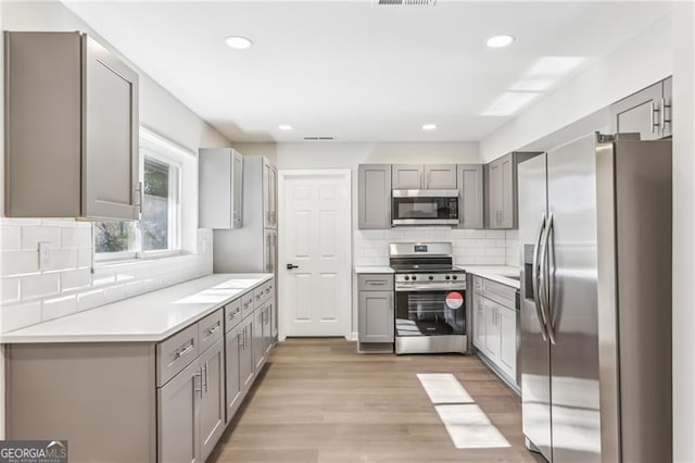 kitchen featuring appliances with stainless steel finishes, light hardwood / wood-style flooring, gray cabinets, and tasteful backsplash