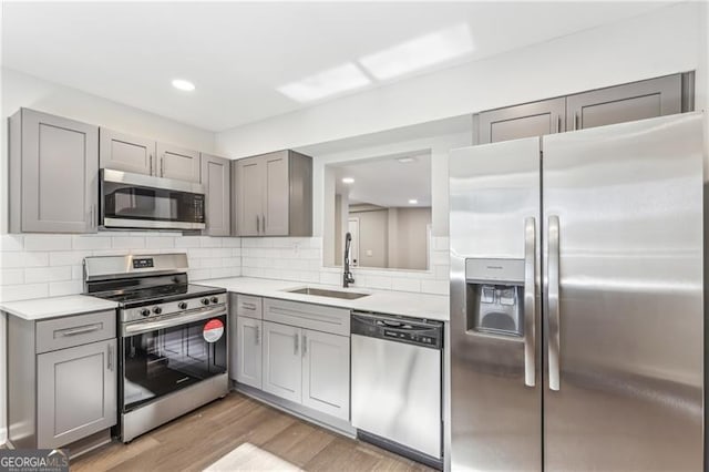 kitchen featuring gray cabinets, stainless steel appliances, sink, light hardwood / wood-style flooring, and backsplash