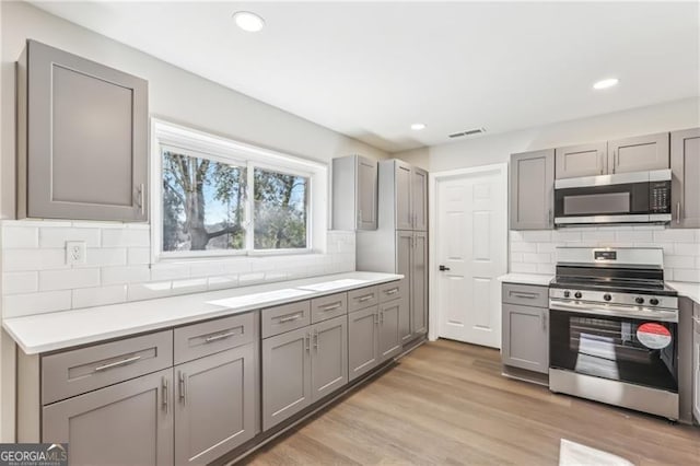 kitchen featuring appliances with stainless steel finishes, light hardwood / wood-style flooring, gray cabinets, and decorative backsplash