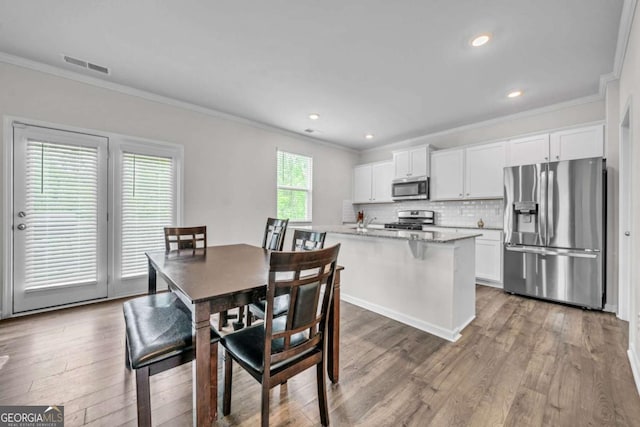 dining area with a healthy amount of sunlight, light hardwood / wood-style floors, and ornamental molding